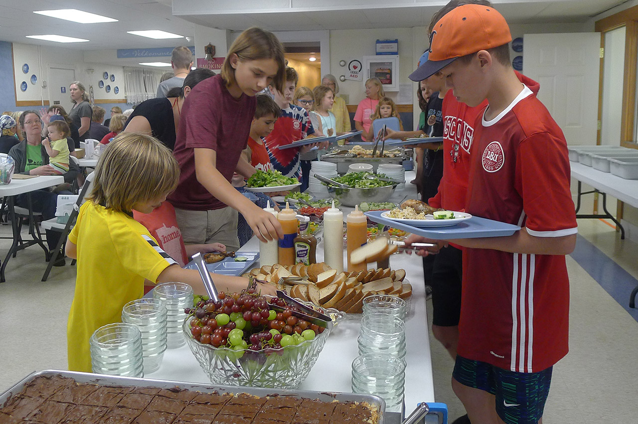 Children select food from a long buffet table in the dining hall at Danebod Family Camp. Three meals and two snacks are provided daily.